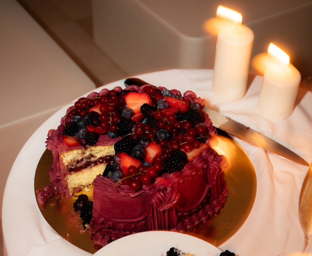 Burgundy buttercream wedding cake with fresh berries and candles on a gold cake board