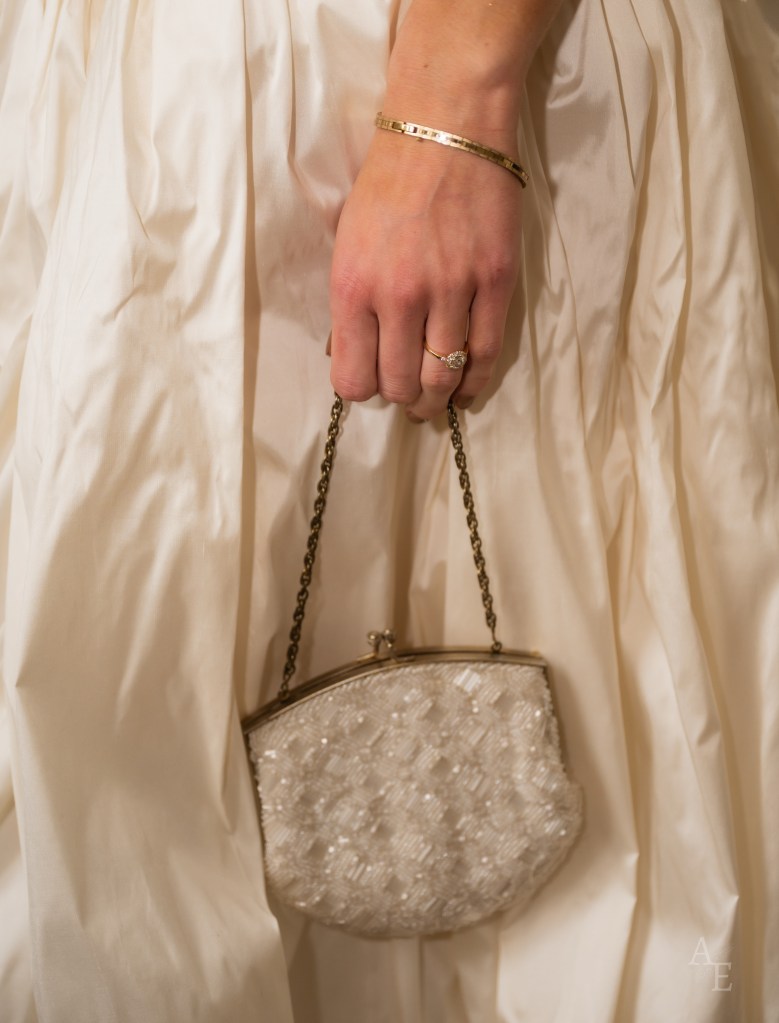 Bride holding vintage beaded clutch purse with satin wedding dress and gold bracelet at Paris wedding